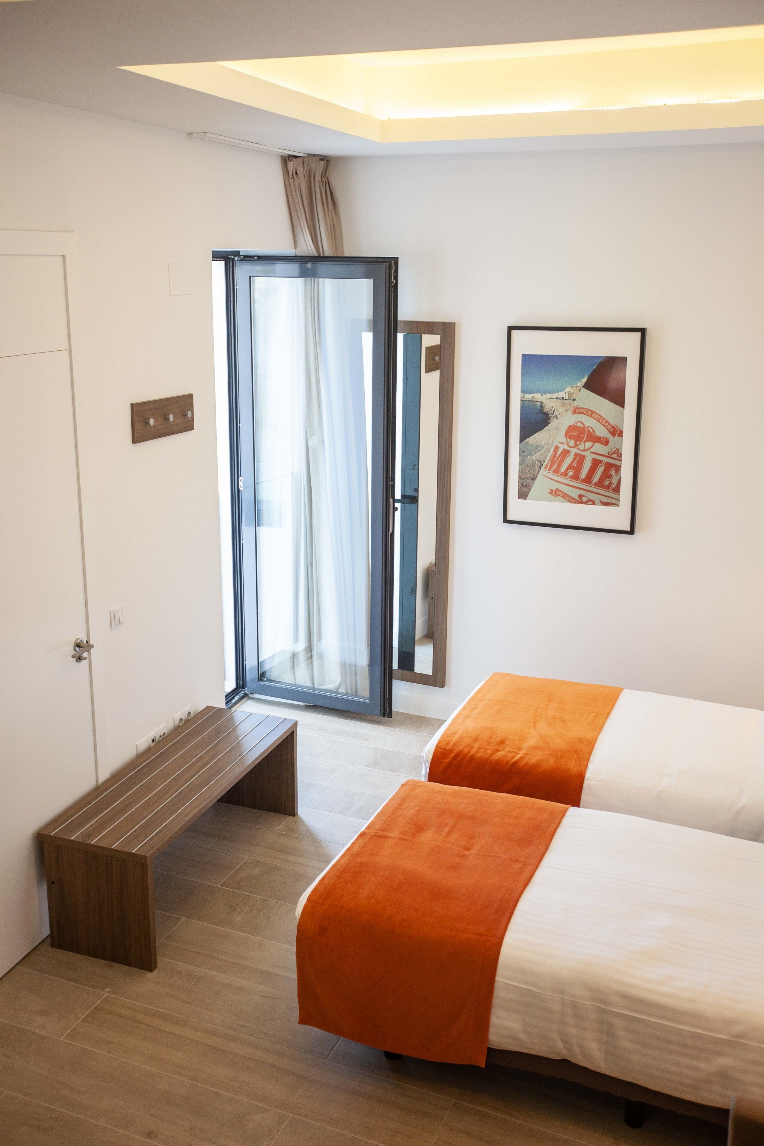 Een hotelkamer met twee bedden, een bank, een schuifdeur en een lijst met een afbeelding aan de muur.