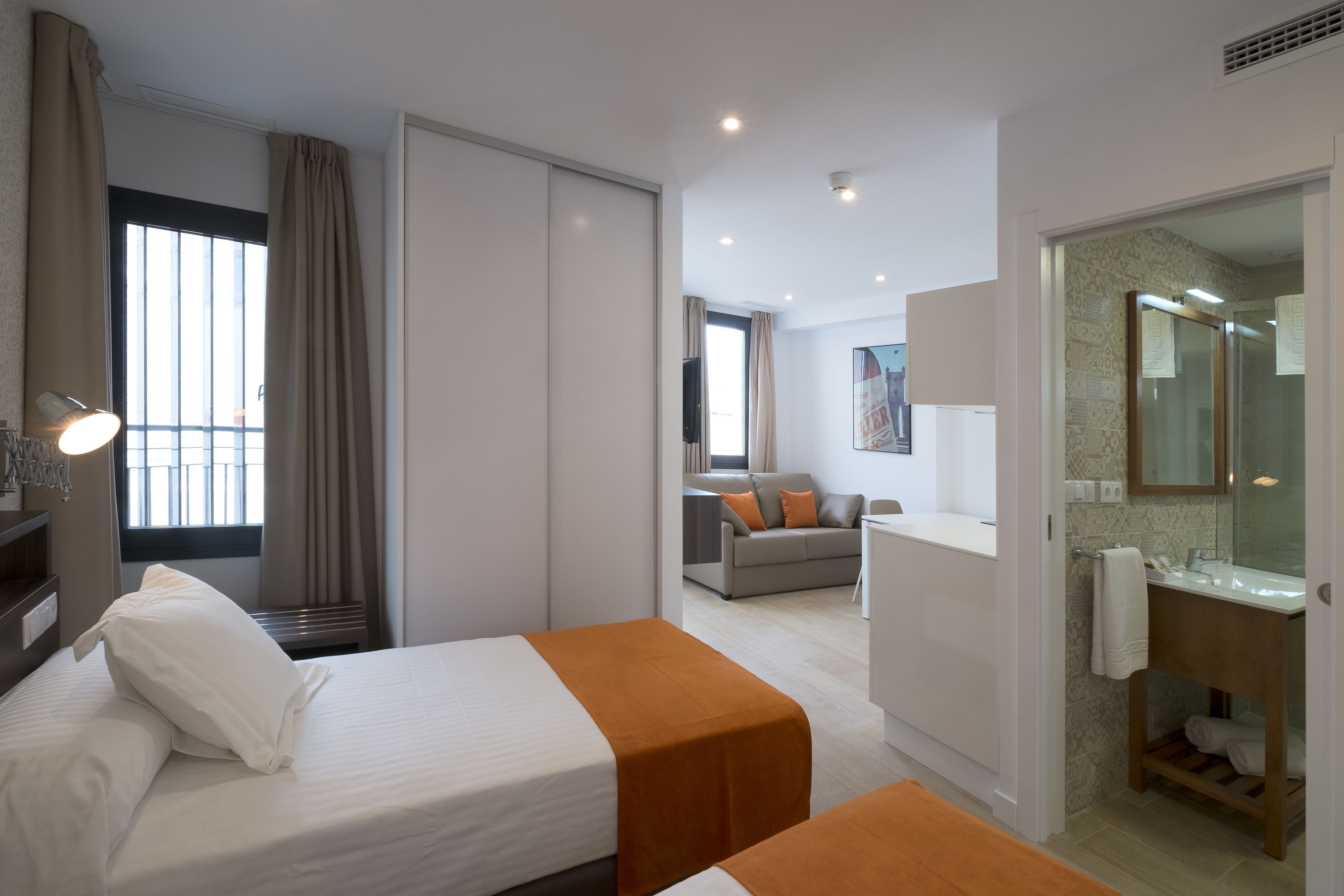 A hotel room with two beds, a bathroom, and a living area with a sofa and a TV.