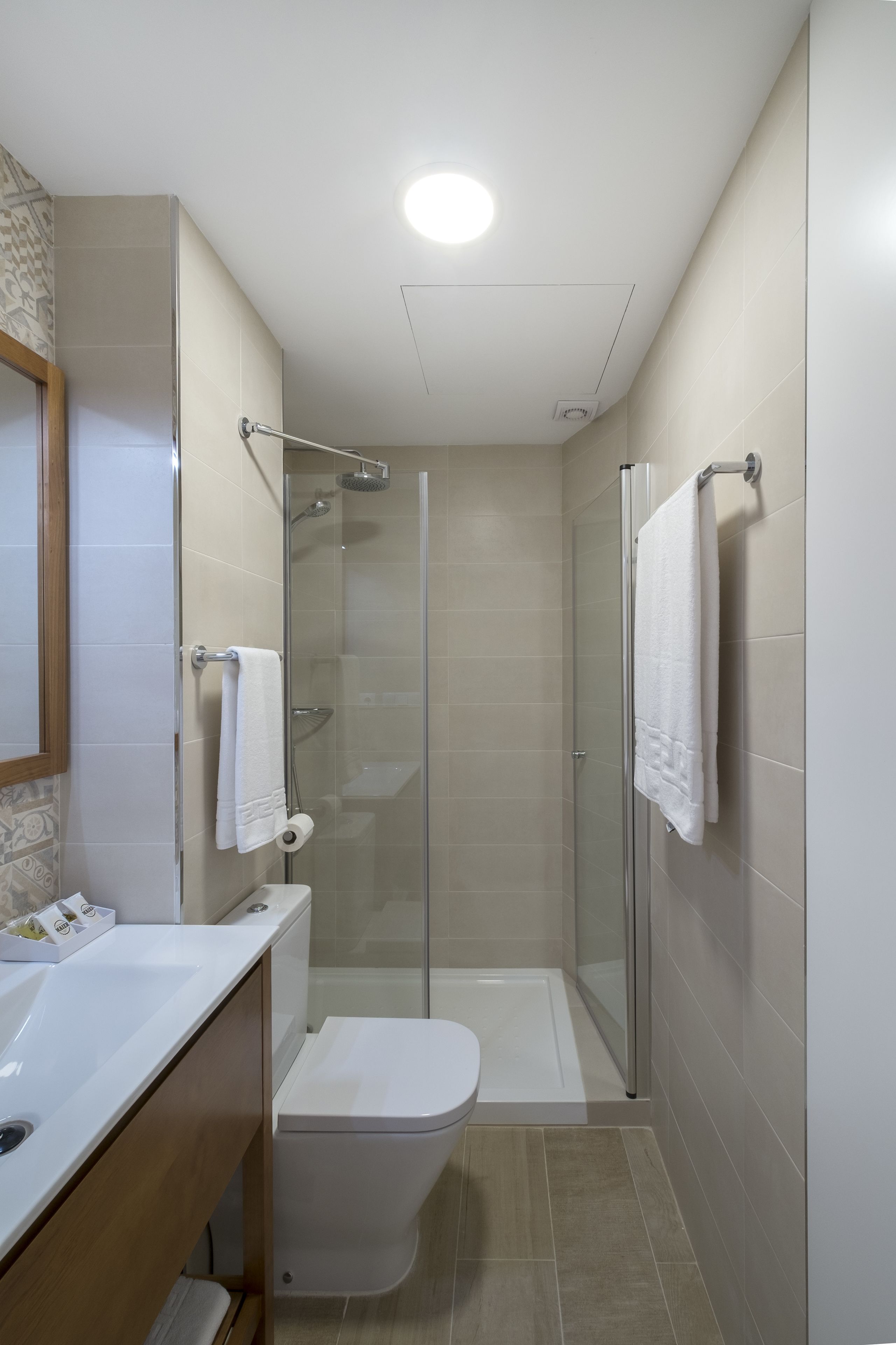 Ein modernes Badezimmer mit einer Glaskabine zur Dusche, einer weißen Toilette und einem Waschtisch mit Spiegel.