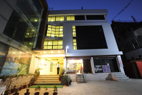 A modern building with a well-lit entrance, steps leading up to the door, and potted plants in front.