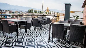 Eine Dachterrasse mit Korbmöbeln, einem gemusterten Boden und Blick auf Berge sowie einen Tempel im Hintergrund.