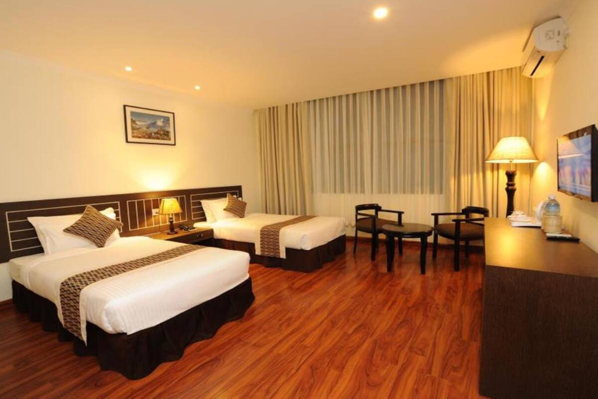 A hotel room with two beds, a desk, a chair, a lamp, and a painting on the wall.