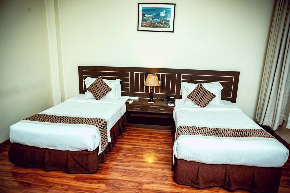 A hotel room with two single beds, a nightstand, a lamp, and a framed picture on the wall.