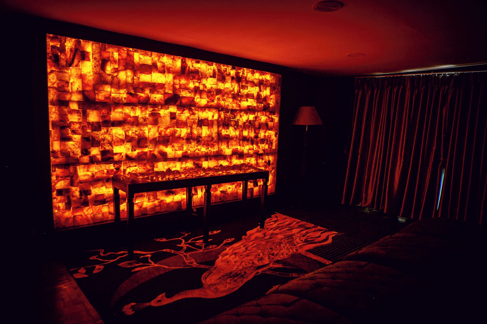 Una habitación tenuemente iluminada con una gran pared de bloques iluminados, una mesita pequeña y una alfombra estampada.