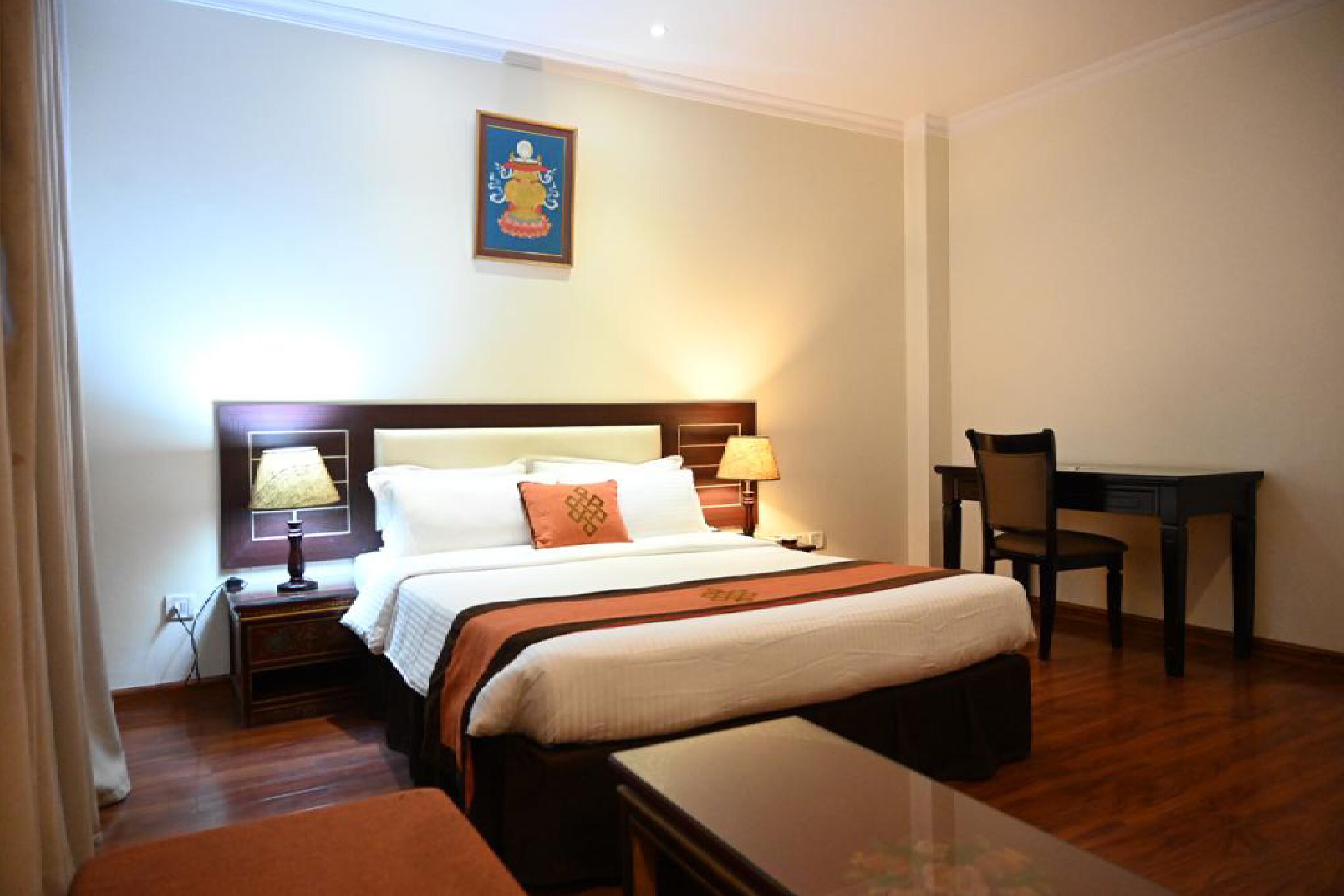 A hotel room with a large bed, two bedside tables with lamps, a desk, and a chair.