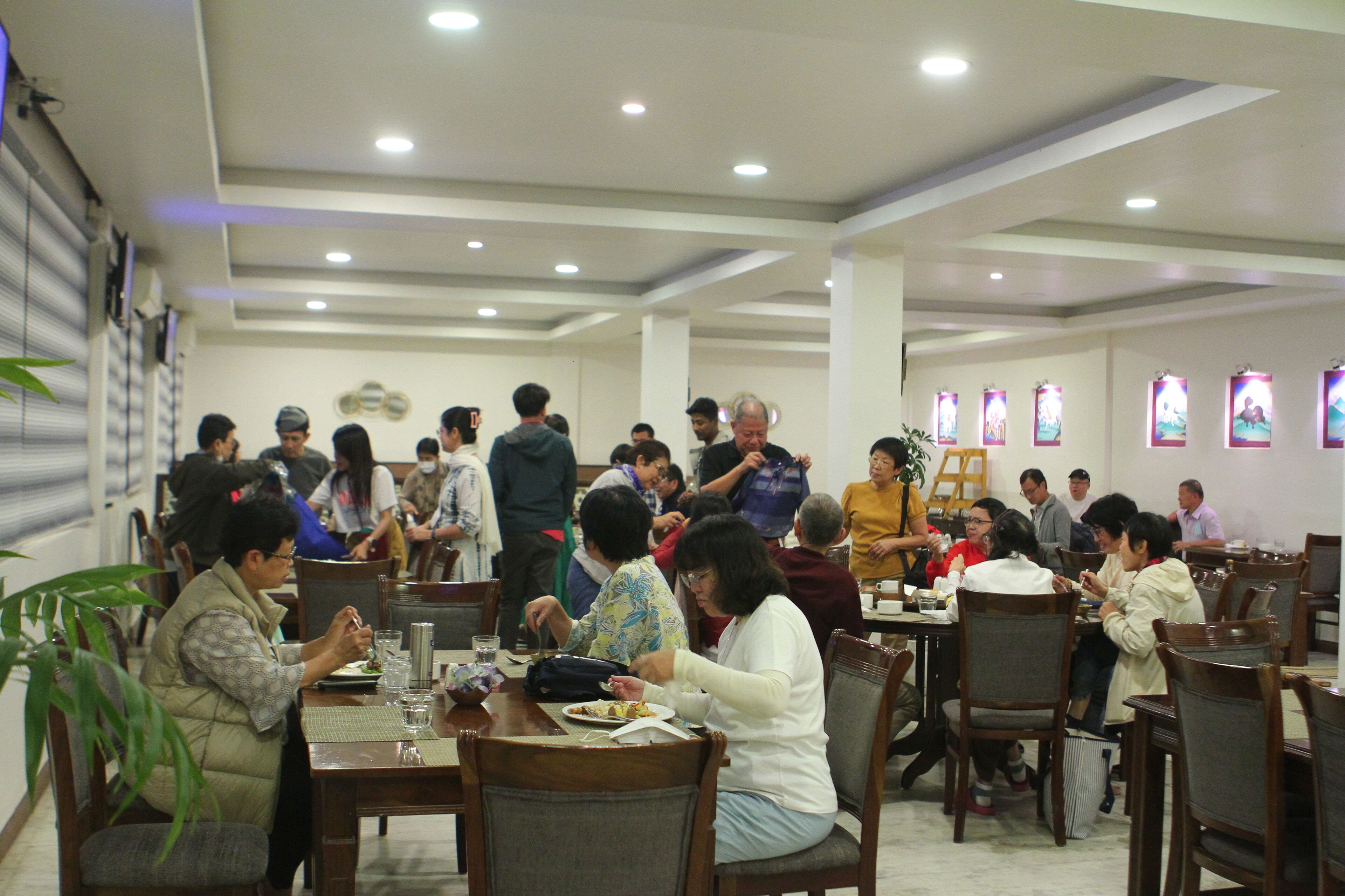 A spacious dining area with multiple tables and chairs, well-lit with ceiling lights, and decorated with wall art.