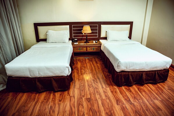 Habitación de hotel con dos camas, suelo de madera, una mesita de noche con lámpara y una pequeña mesa.