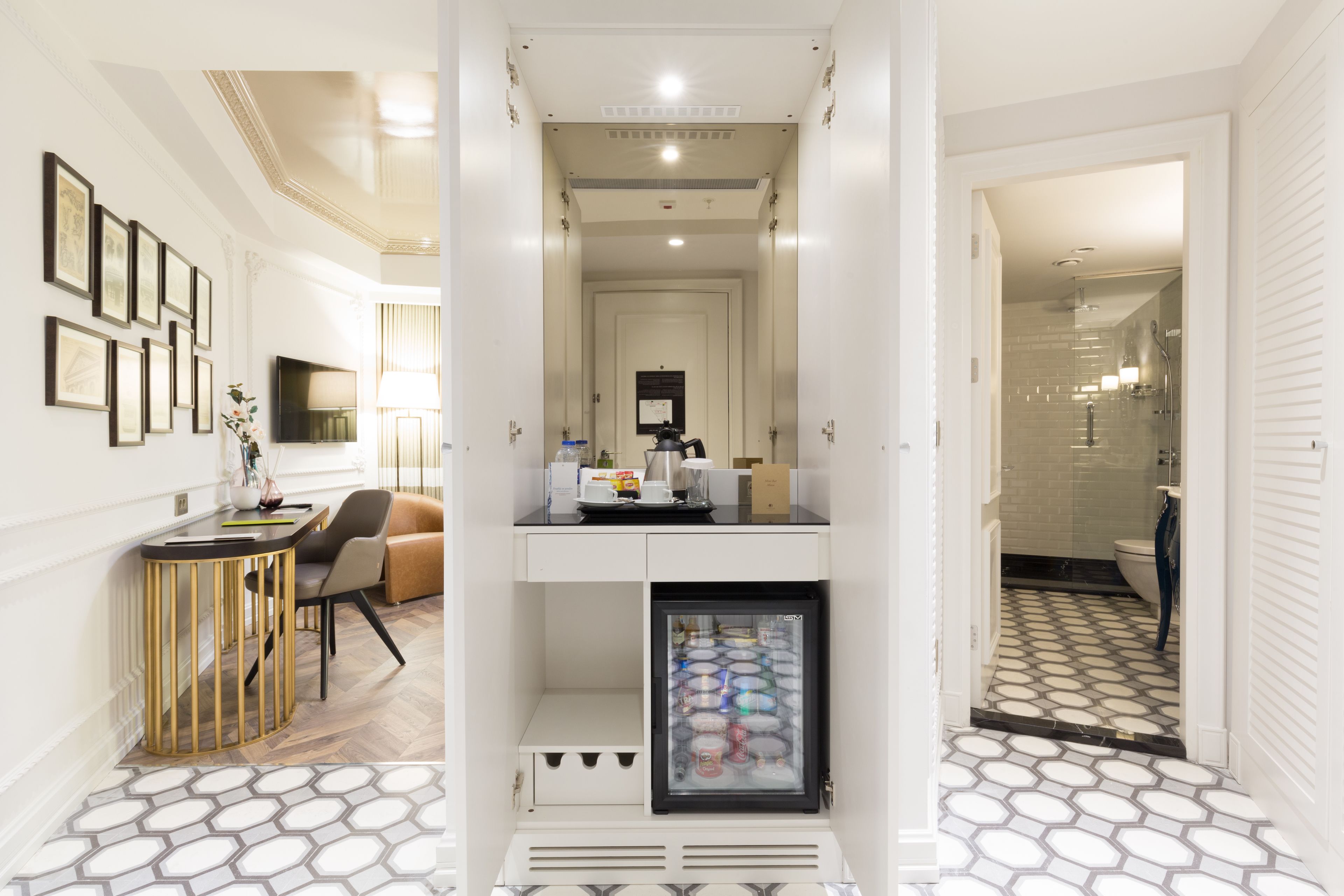 A hotel corridor with a seating area, a refrigerator, and a bathroom visible through an open door.