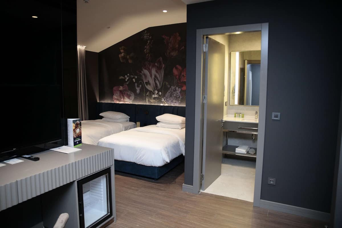 Une chambre d’hôtel moderne, dotée d’un grand lit, d’un bureau et d’une salle de bain visible à travers une porte ouverte.