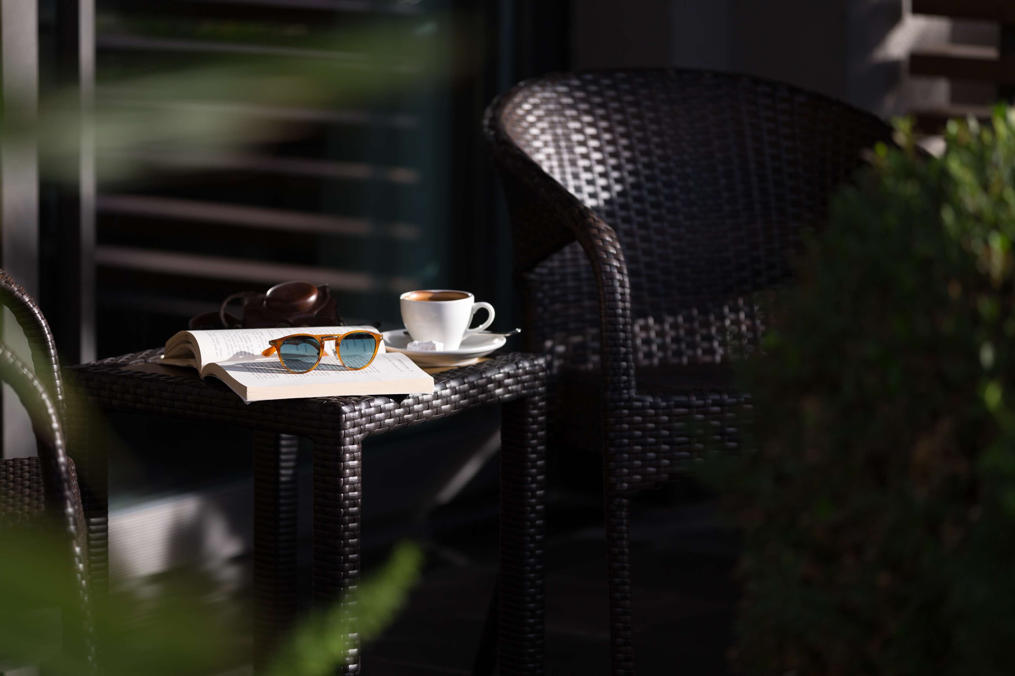 A wicker chair with a cup of coffee and sunglasses on a table.