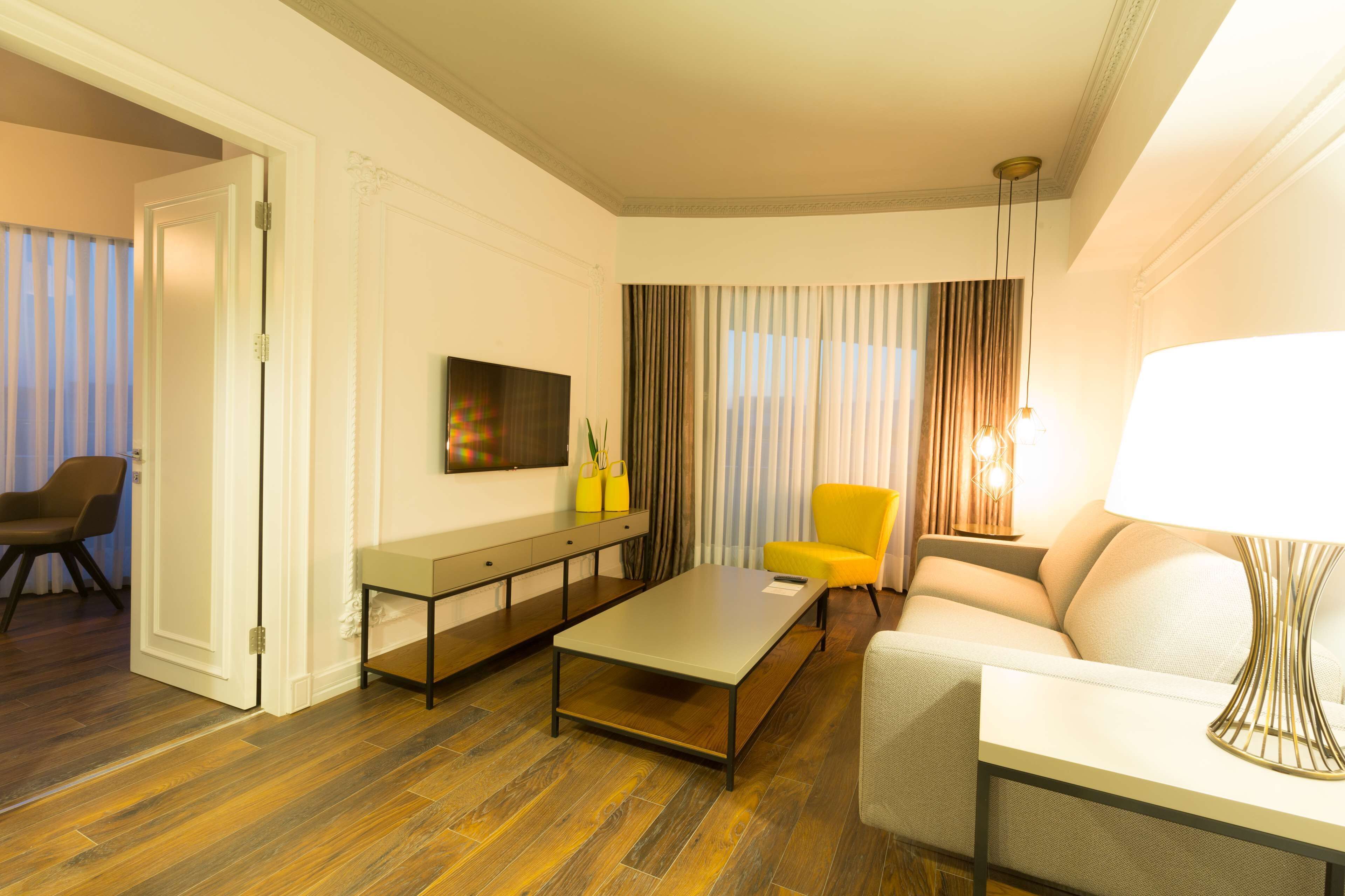A hotel room with a sofa, a coffee table, a TV, and a lamp.