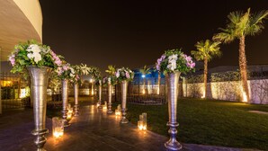 A nighttime outdoor area with a pathway lined with tall metal columns, each topped with floral arrangements.