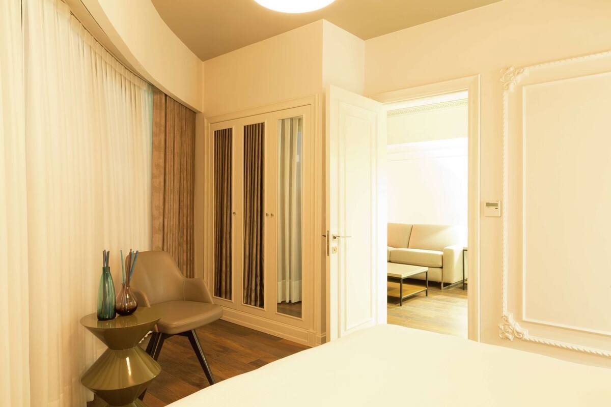 Une chambre d’hôtel comprenant un lit, une chaise, une petite table, une armoire et donnant sur un espace de vie.