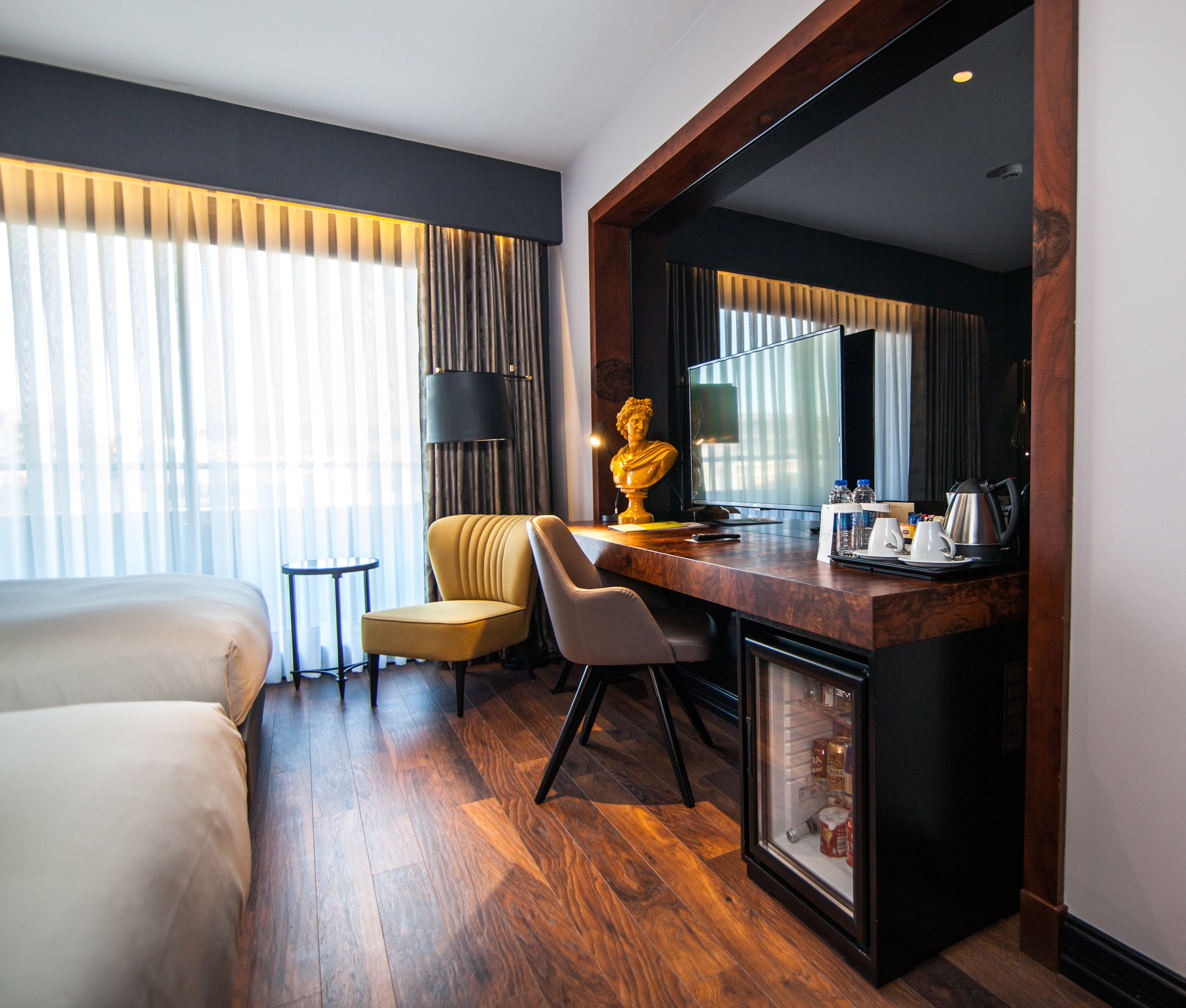Een hotelkamer met een bed, een bureau met een computer, een stoel en een kleine koelkast.
