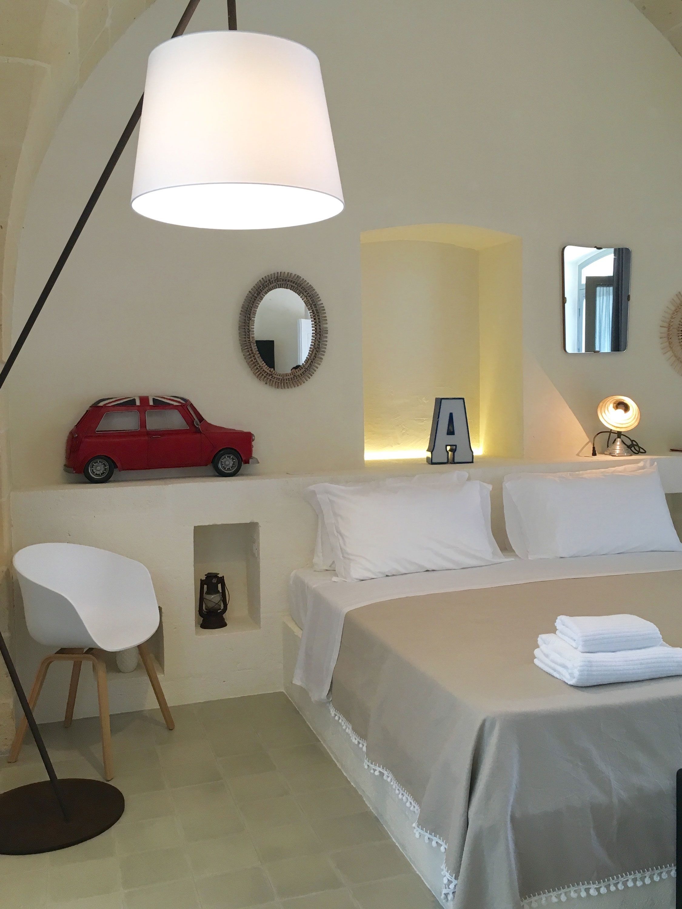 Une chambre à coucher avec un lit, une chaise, une lampe, un miroir et une voiture jouet.