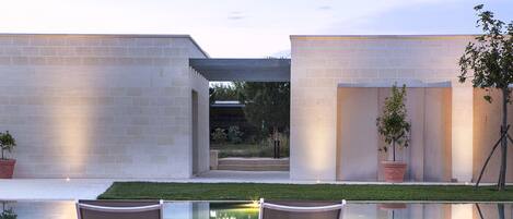 A modern outdoor pool area with two lounge chairs, a stone wall, and a small garden.