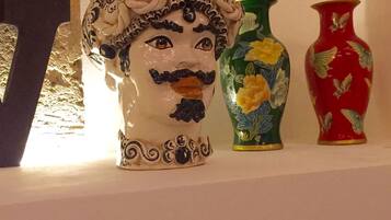 Uma escultura de cabeça em cerâmica com uma coroa, um vaso verde com flores amarelas e um vaso vermelho com desenhos de borboletas.