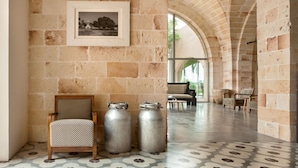 A room with a stone wall, a framed picture, a wooden chair, and metal containers. - Vinilia Wine Resort (Manduria)