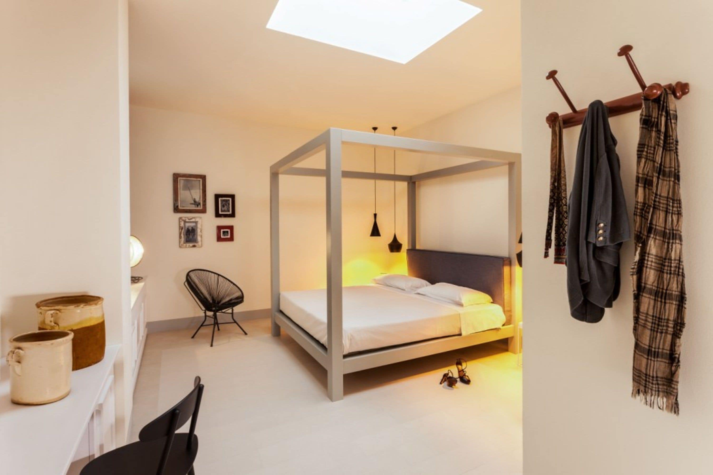 A modern bedroom with a four-poster bed, a chair, a desk, and a coat rack.