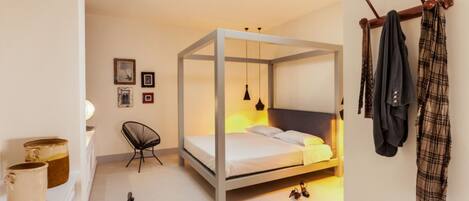 A modern bedroom with a four-poster bed, a chair, a desk, and a coat rack.