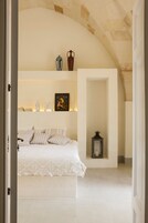 Un dormitorio con una cama, una mesita de noche, un estante empotrado con objetos decorativos y un arco de piedra.