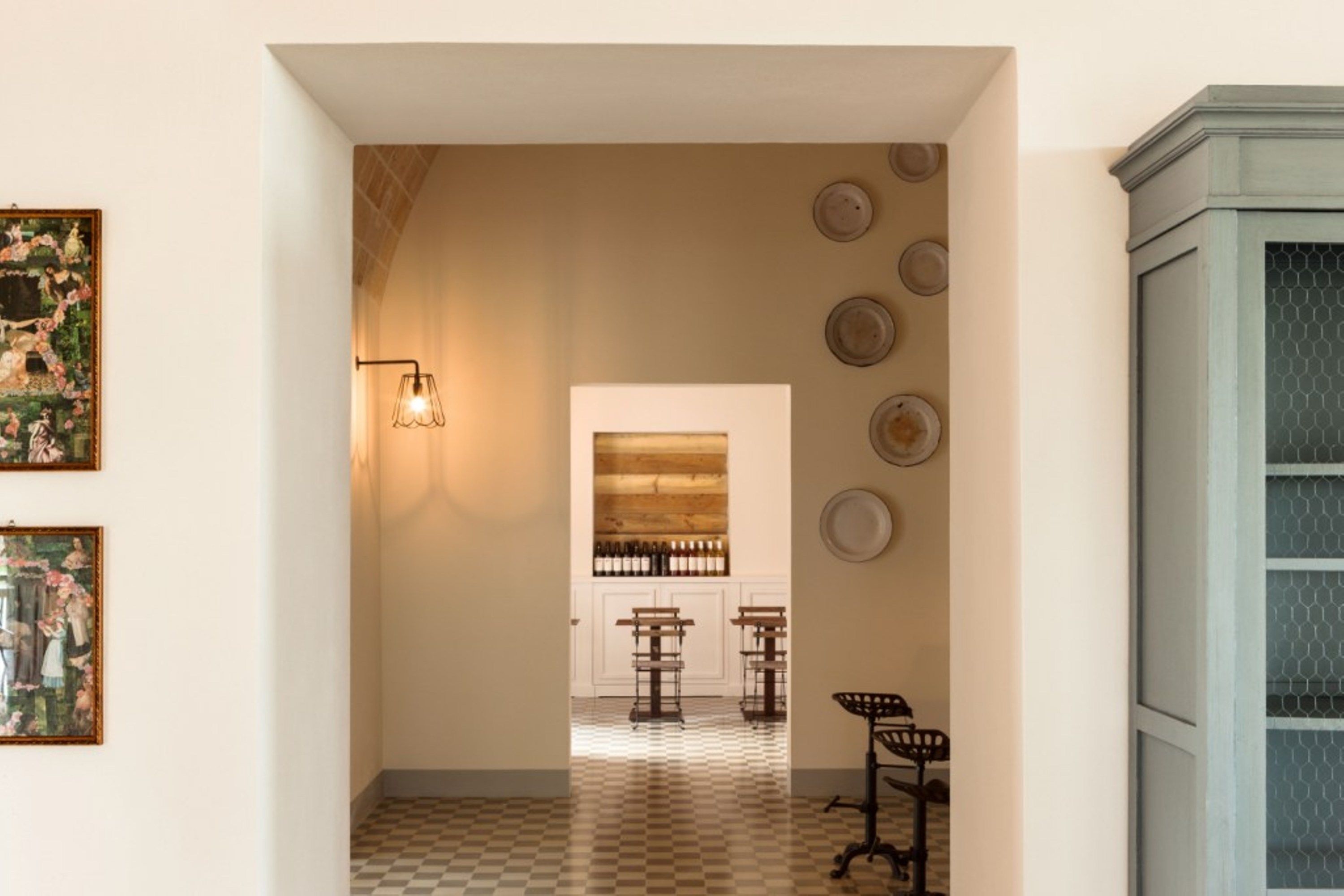 Un couloir avec un sol à carreaux, un luminaire fixé au mur et une série d’assiettes accrochées au mur.