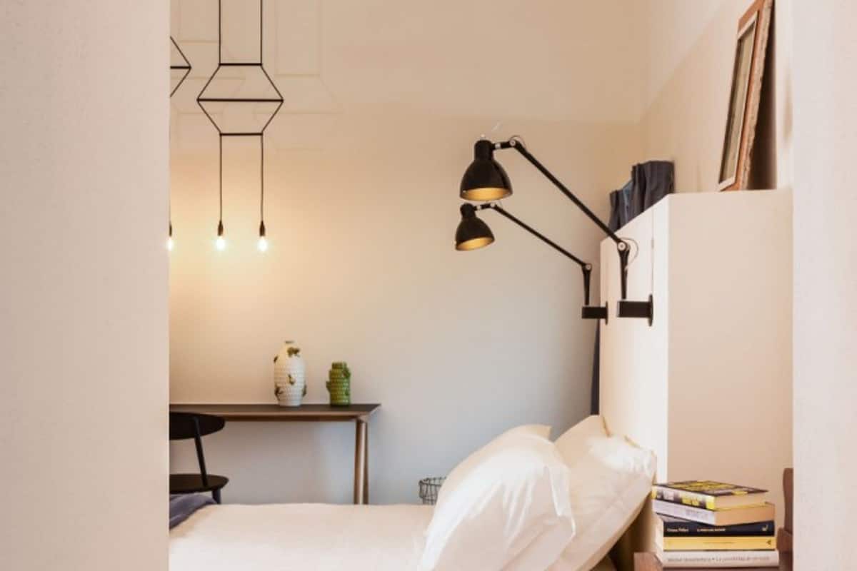 Un dormitorio pequeño y ordenado con cama, mesita de noche, lámpara y escritorio con silla.