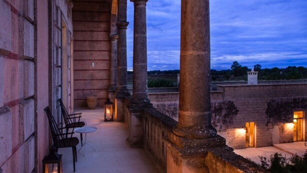 An outdoor corridor with stone columns, a seating area with chairs and a table, and lanterns providing light. - Vinilia Wine Resort (Manduria)