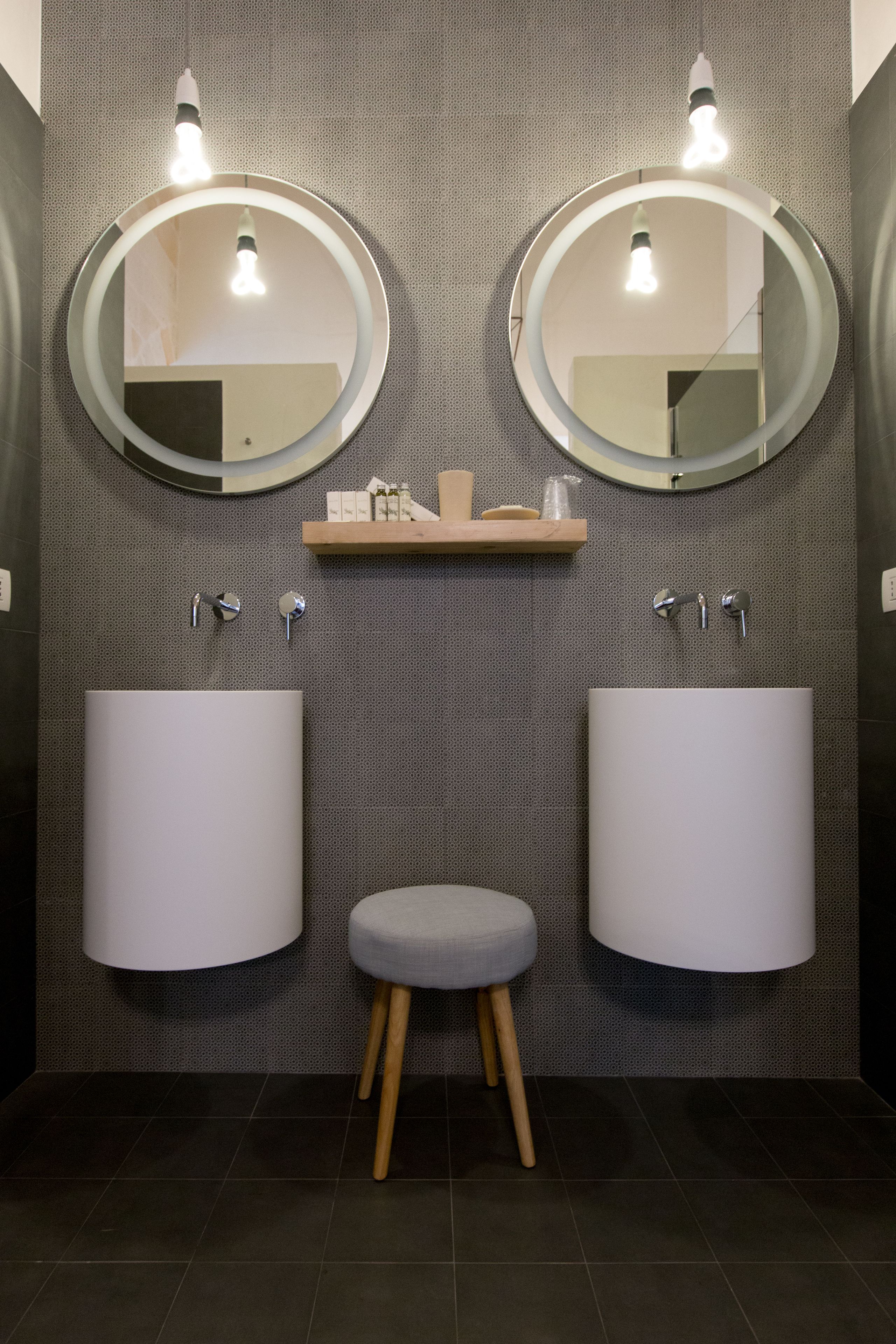A modern bathroom with two round mirrors, a central shelf with toiletries, and two large sinks.