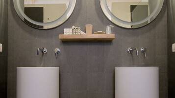 A modern bathroom with two round mirrors, a central shelf with toiletries, and two large sinks.