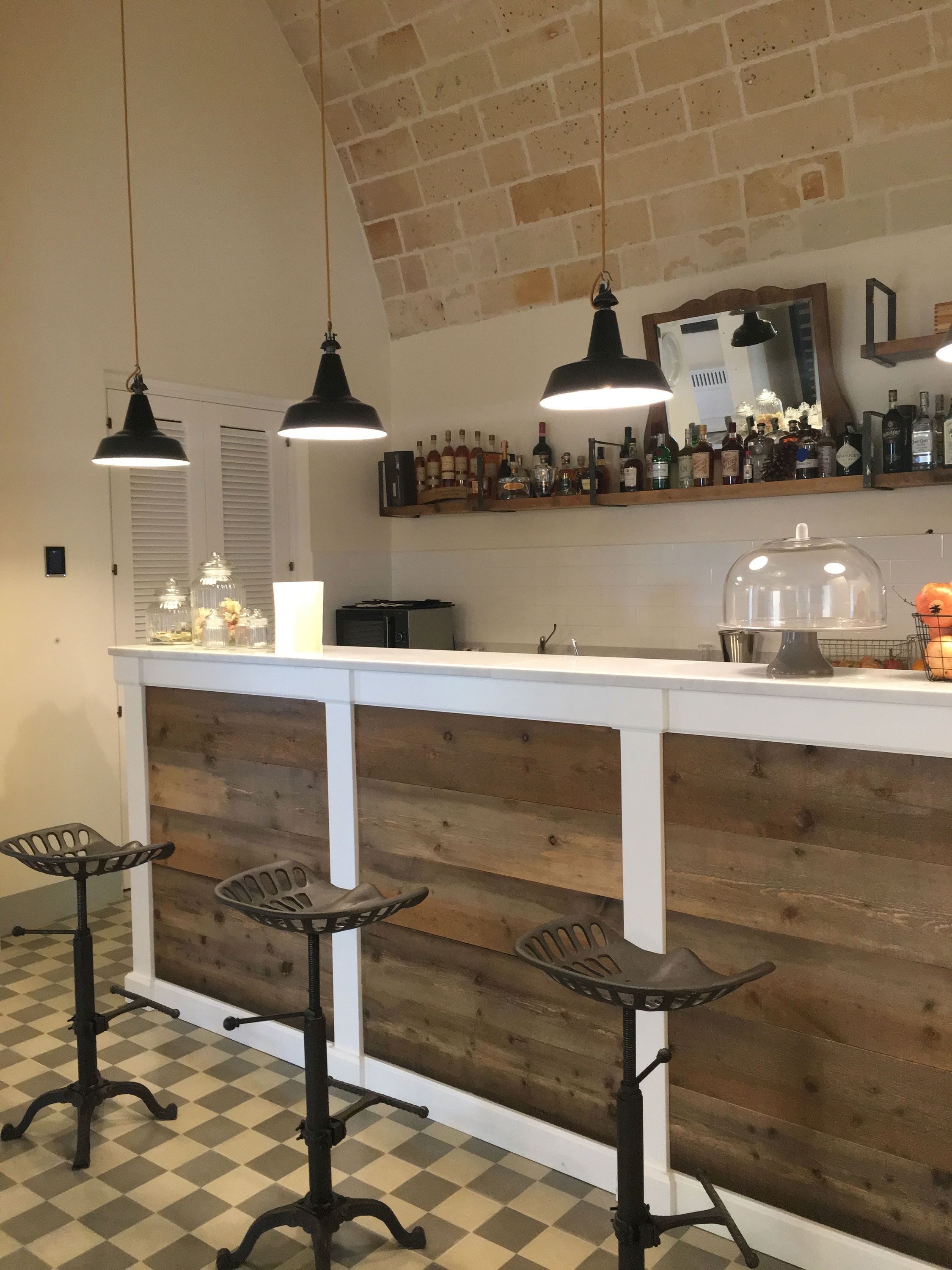 Una zona de bar con paneles de madera, una barra blanca y tres taburetes negros.
