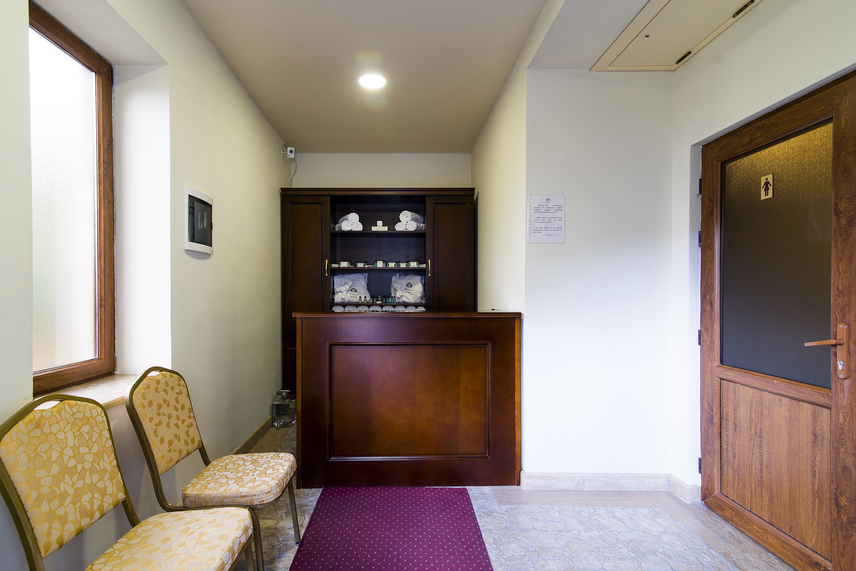 Un pasillo con un mostrador de recepción de madera, una alfombra morada y dos sillones estampados.