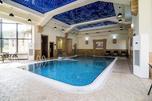 An indoor swimming pool with a starry ceiling, stone flooring, and wooden walls.