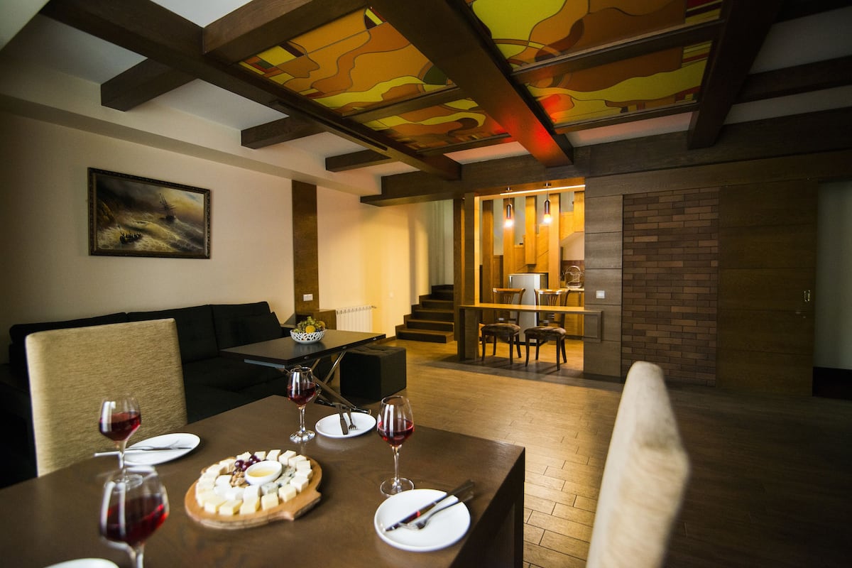 A dining area with a wooden table set for a meal, featuring a cheese platter and wine glasses.