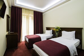 A hotel room with two beds, a nightstand, a TV, and a window with curtains.