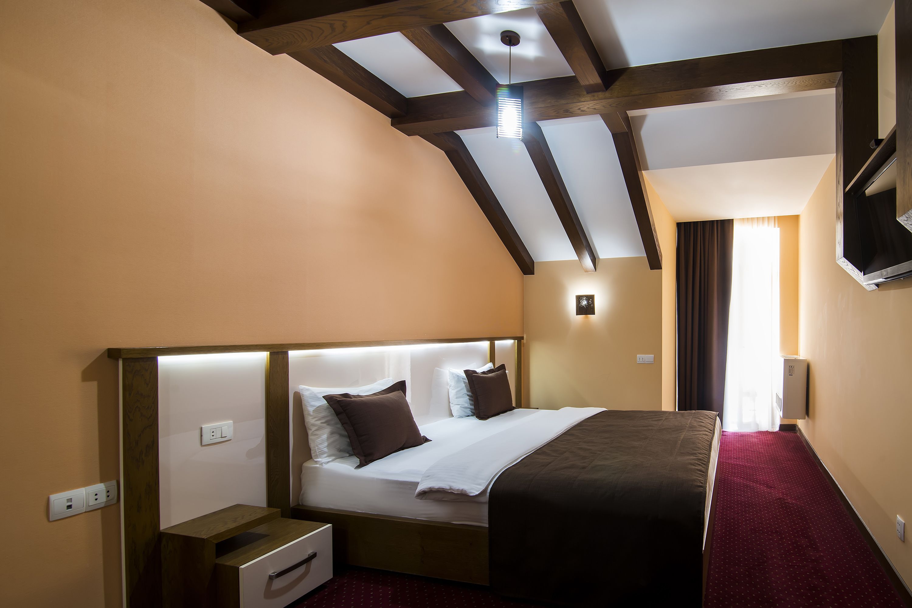 Una camera d'albergo con un letto grande, un comodino, una televisione a schermo piatto montata a parete e un soffitto con travi a vista.