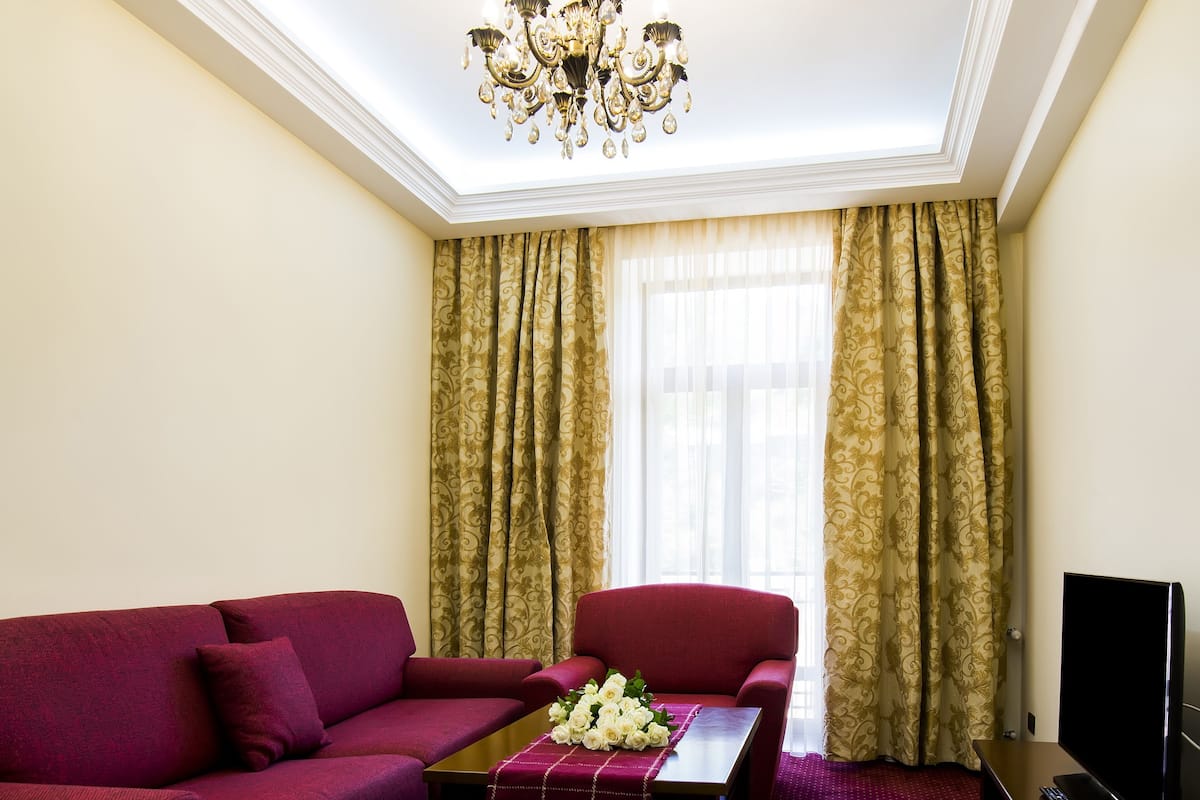 A living room with a red sofa, a matching armchair, a coffee table with flowers, a TV, and a chandelier.
