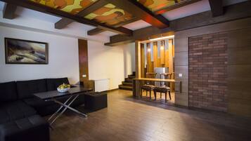 A modern living room with a black sofa, a dining table, and a staircase leading to an upper level.