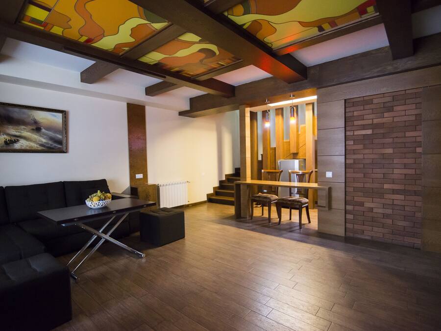 A modern living room with a black sofa, a dining table, and a staircase leading to an upper level.