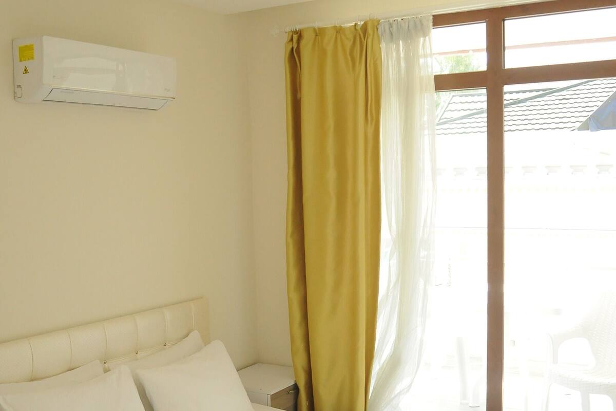 A hotel room with a bed, a window with curtains, a bedside table, and a wall-mounted air conditioner.