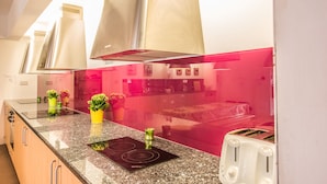 A modern kitchen with a granite countertop, stainless steel appliances, and a red accent wall. - The Old Mill Holiday Hostel (Westport)