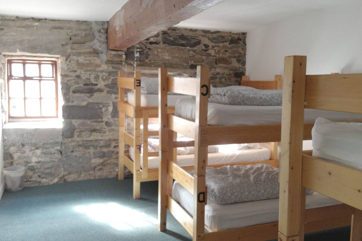 A room with bunk beds, a stone wall, and a window with bars.