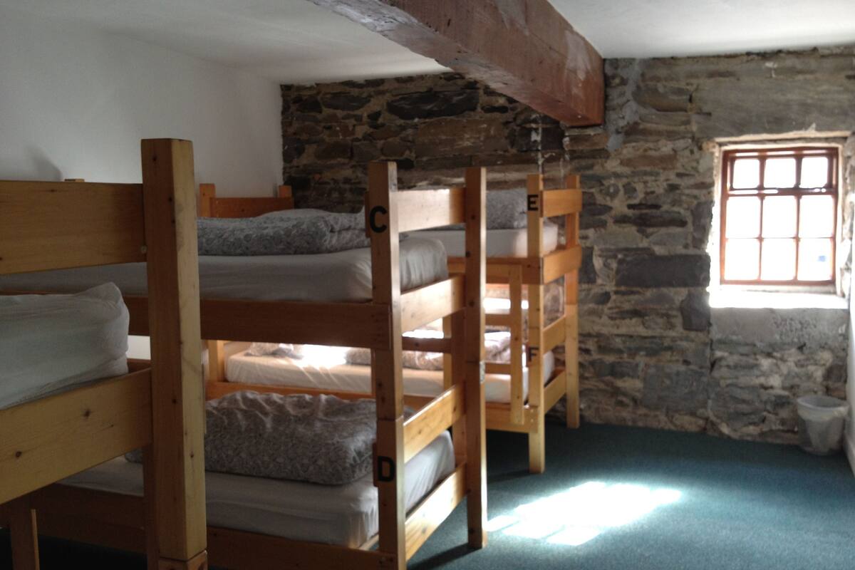 A dormitory room with bunk beds, stone walls, and a small window.