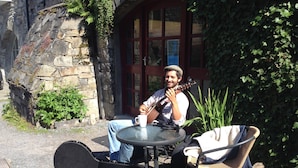A person sitting at a round table with a guitar, a white mug, and a wicker chair. - The Old Mill Holiday Hostel (Westport)