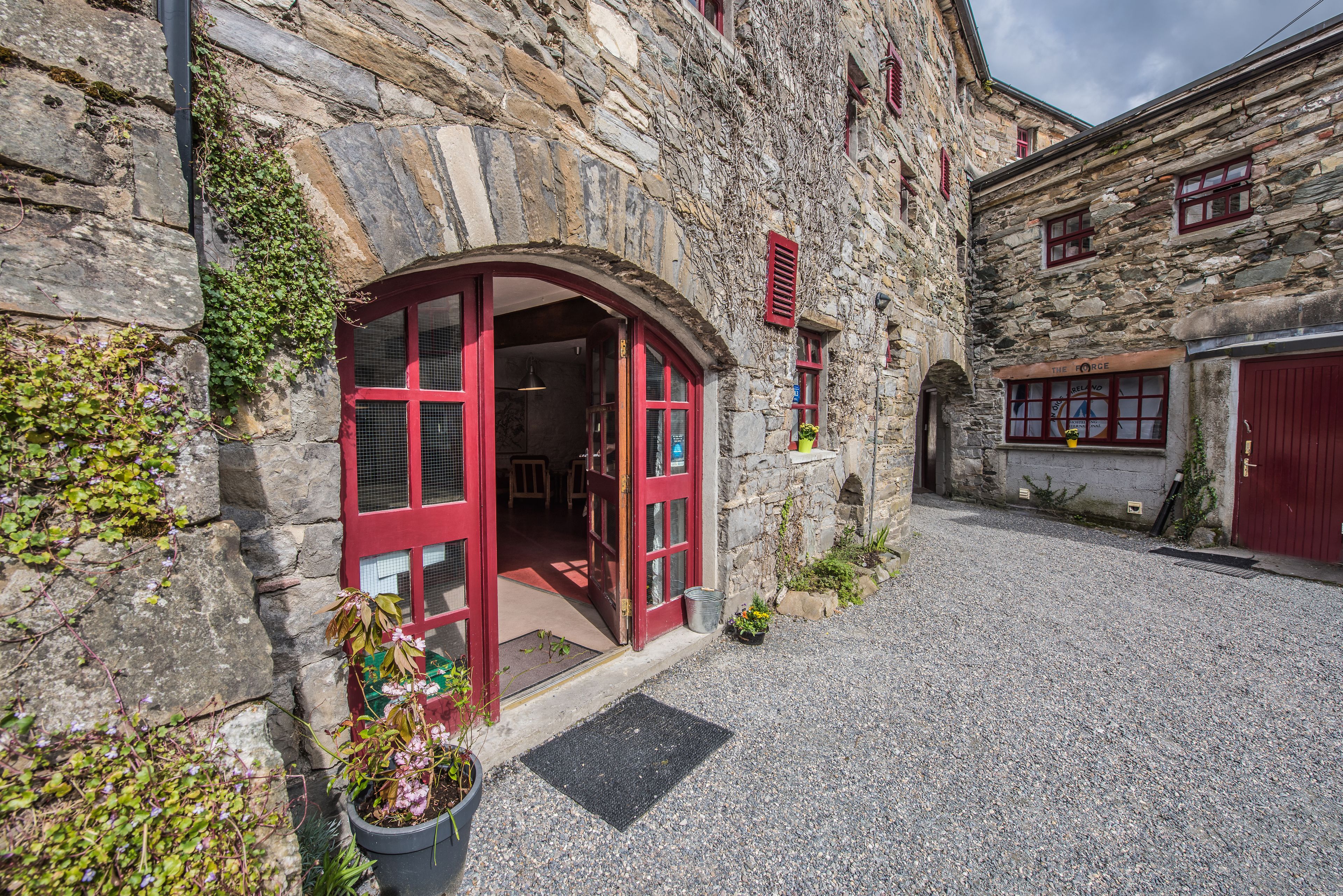 A stone building with a red door and windows, a gravel driveway, and a potted plant.