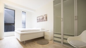 A modern bedroom with a bed, bedside tables, a chair, and a glass door closet. - Bjørvika Apartments - Sølvbergsgata 17 (Stavanger)