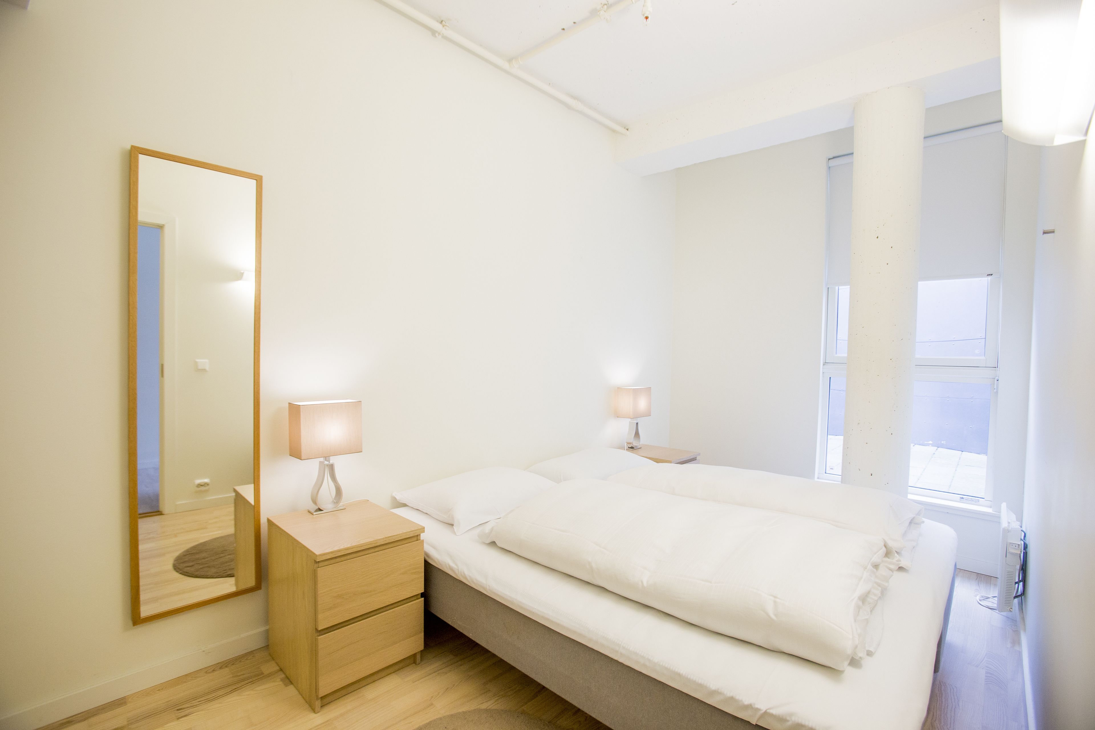 A bedroom with a single bed, bedside tables, a mirror, and a window.