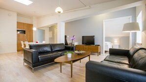 A modern living room with a black leather sofa, a wooden coffee table, and a flat-screen TV. - Bjørvika Apartments - Sølvbergsgata 17 (Stavanger)