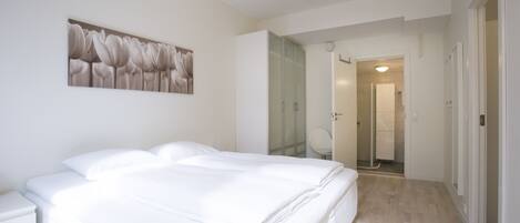 A bedroom with a large bed, a nightstand, a wall-mounted artwork, and a bathroom visible through an open door.