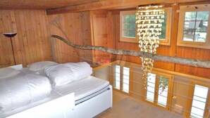 Een slaapkamer in een houten chalet, met een bed, een kroonluchter en grote ramen.